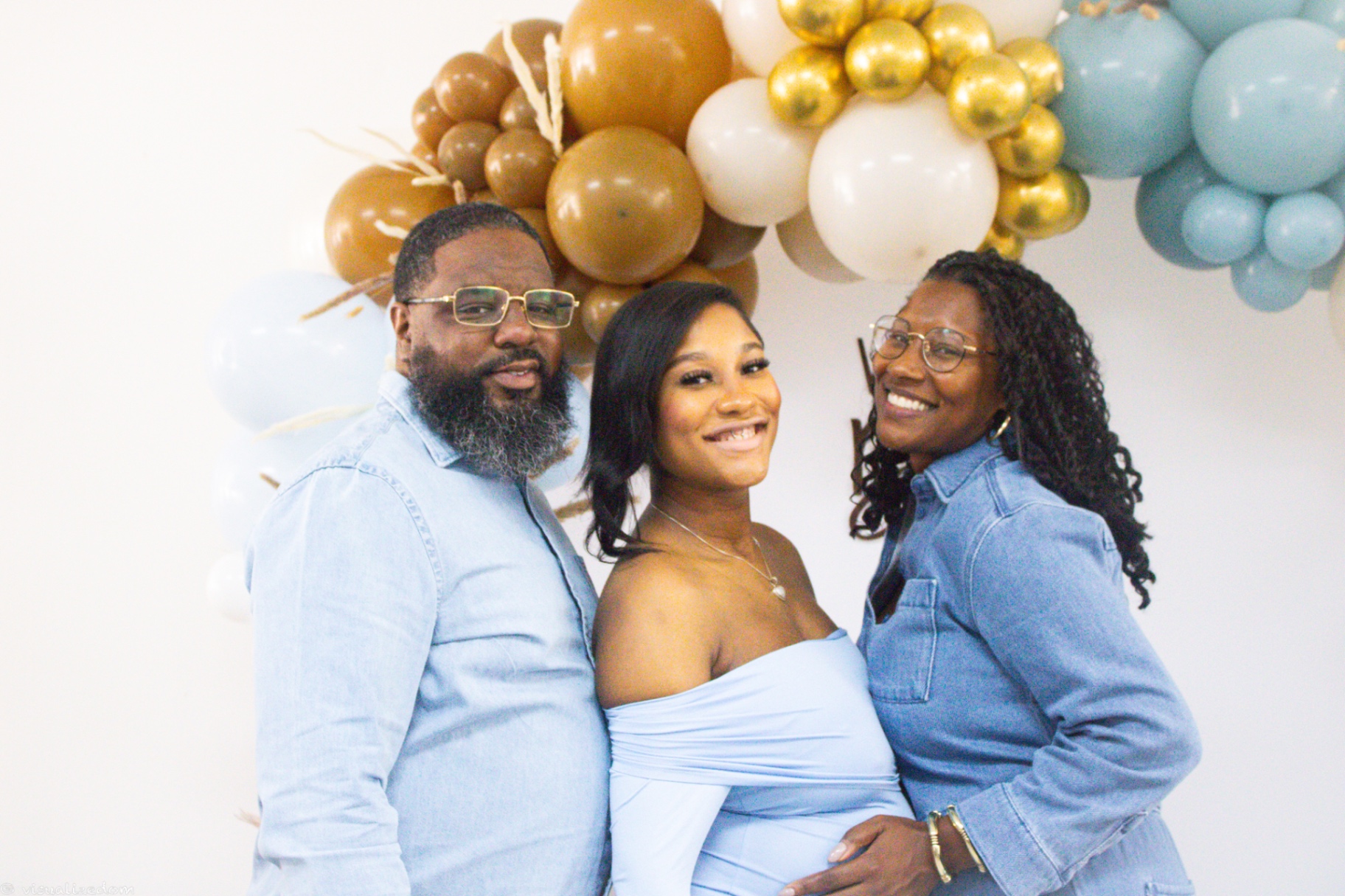 Family portrait smiling in front of a blue and gold balloon arch at a graduation party