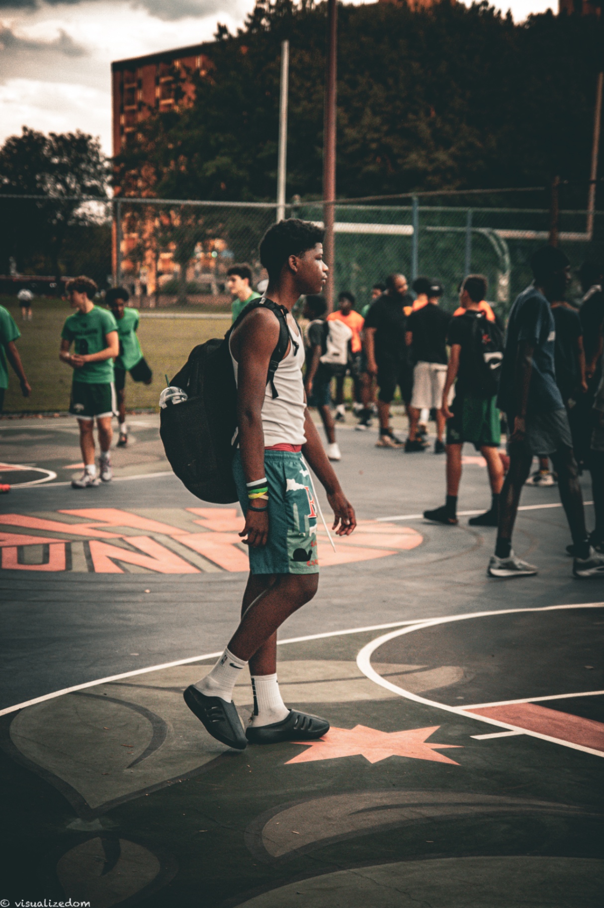 High school athlete carrying a backpack while walking off an outdoor basketball court