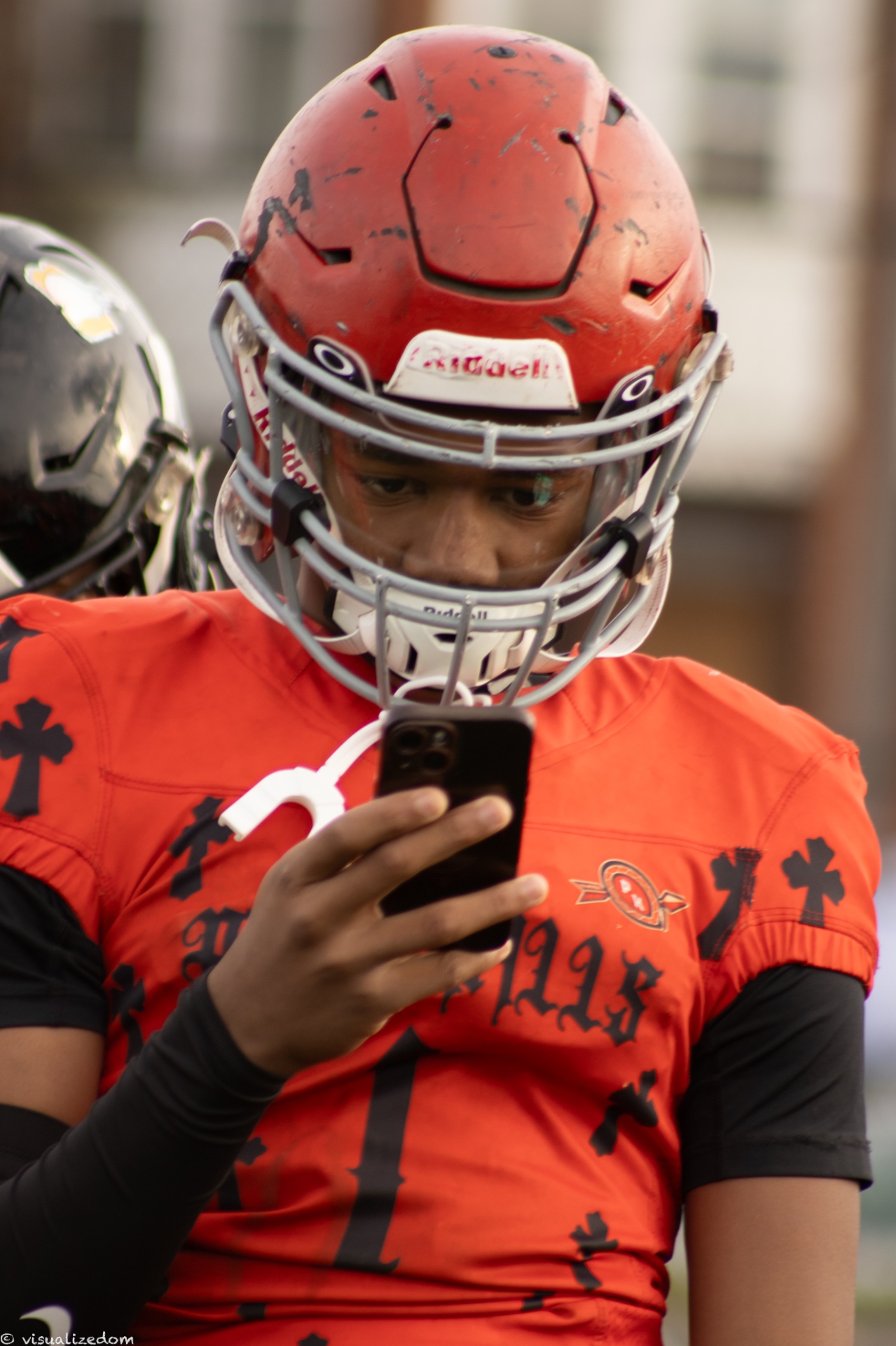 High school football player in an orange jersey checking his phone before the game